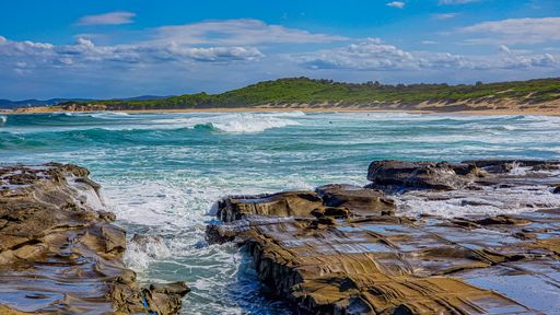 Beautiful view of the wavy sea hitting the rocky beach under the blue sky