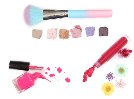 A top view shot of spilled Nail polish, Liquid Lipstick, and Broken Eye Shadow with a brush isolated on a white background