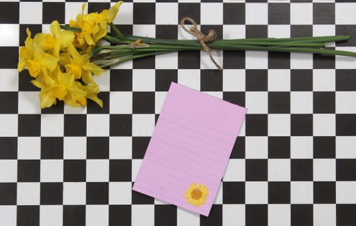 A top view of Yellow Daffodils and Notepaper on Checkered Background