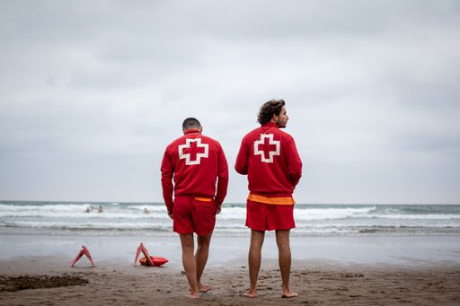 Color photo of two lifeguards at the beach, with a strong red to it