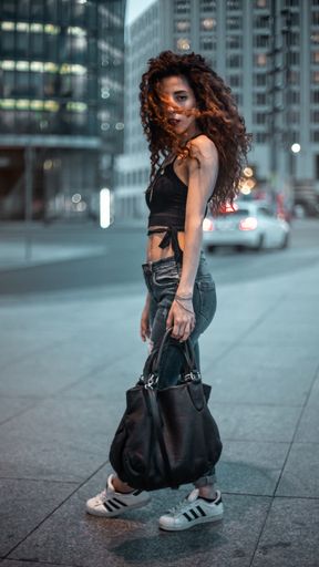 A vertical shot of a Caucasian young woman posing in jeans and sneakers, in the streets of Berlin, Germany