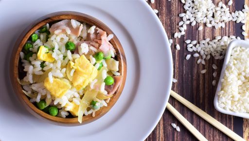A top view shot of a plate full of rice three delights, and chopsticks on a wooden table