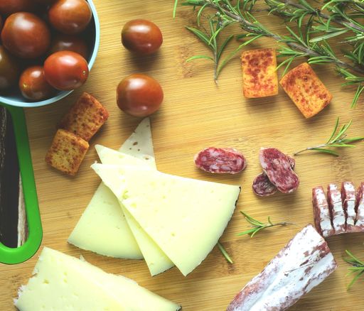 A top view shot of a wooden table with sausage, cheese, crackers, rosemary, and tomatoes