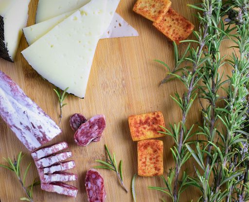 A top view shot of a wooden table with sausage, cheese, crackers, and rosemary