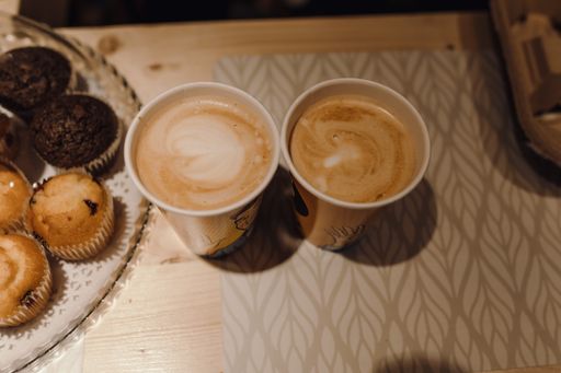 A top view of two coffee cups with a cappuccino and some muffins on the table