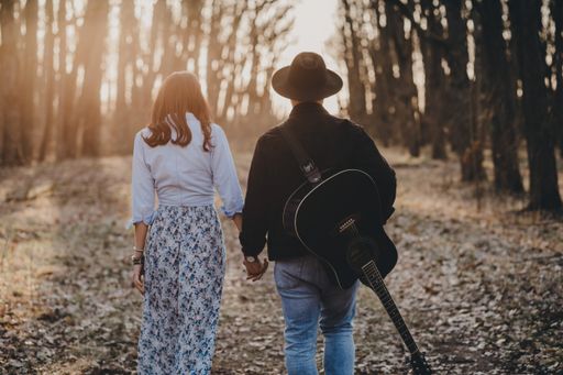 A back view of a romantic couple walking in the forest with a guitar