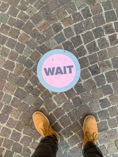 A round sticker saying wait on the cobblestone ground