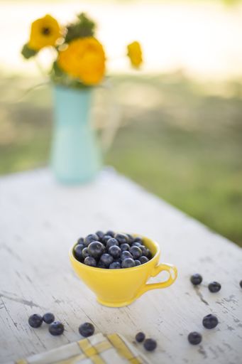 A vertical shot of fresh blueberries in a yellow cup on a wooden surface with a blurred background