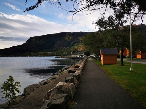 A shot of a lake coastline near small orange houses with grassy hills in the background