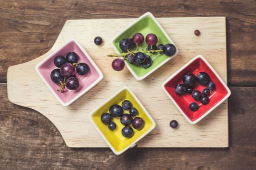 A closeup shot of ripe black currant in small colored bowls on a wooden board