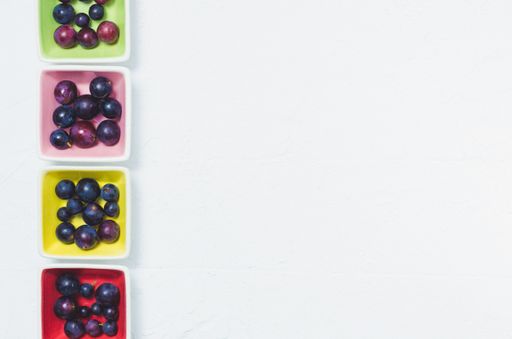A closeup shot of ripe black currant in colored bowls isolated on a white background with copy space
