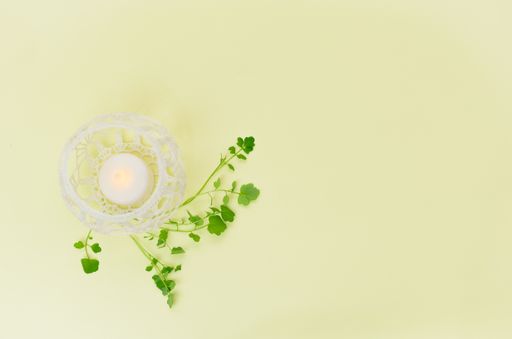 A flameless LED candle inside a white vase ball with green leaves on a beige surface with copy space