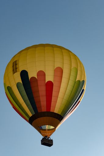 A low angle shot of a brightly painted hot air balloon in flight with blue sky in the background