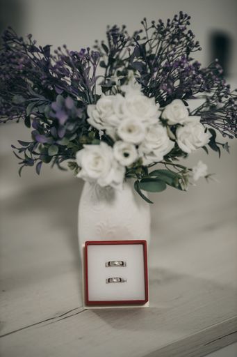 A vertical shot of a red box with silver wedding rings near a vase with flowers