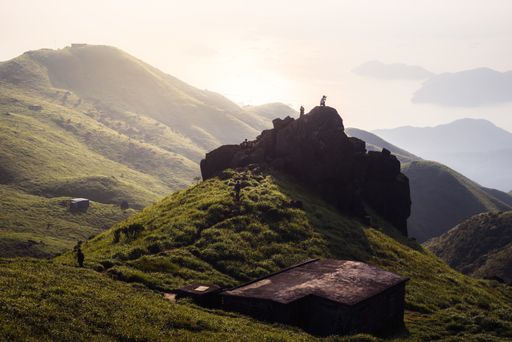 A closeup shot of men standing on rocks on a hill covered in greenery with a sea on the background