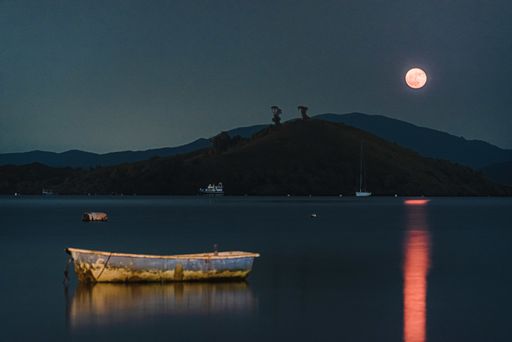 A lake with a fool moon's pink reflection on it and a wooden boat