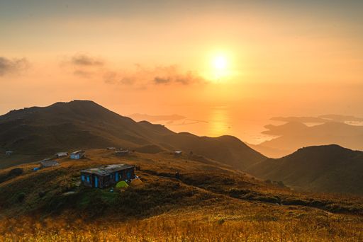 A beautiful shot of a field with houses on hills under an orange sky at sunset