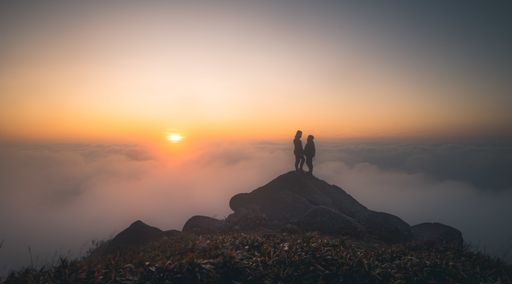 A silhouette of a loving couple standing on a stone surrounded with fog during the sunset
