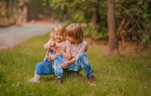 A shallow focus of two siblings sitting on a tree stump in the forest