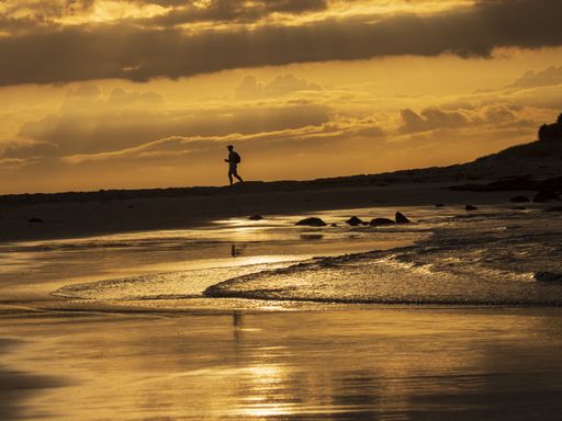 A silhouette of a male running on the rocky shore of the sea under the golden sunset sky