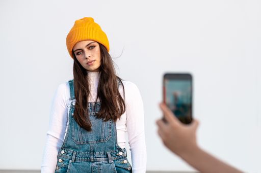 A young Caucasian female wearing denim pants, white shirt and a yellow hat posing against a white wall