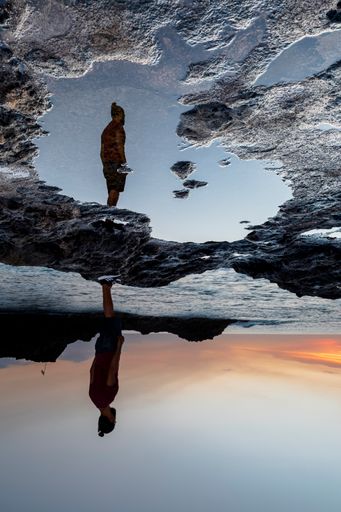A reflection of a standing man in a puddle of water under the sunset