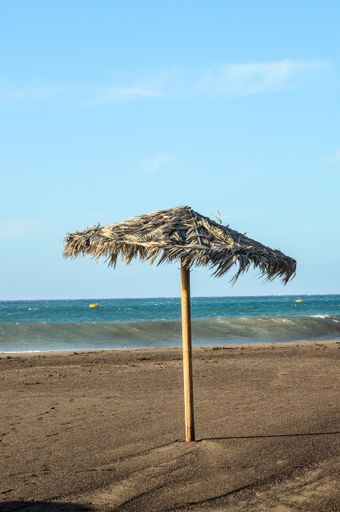 A vertical shot of an umbrella on a beach under the clear skies