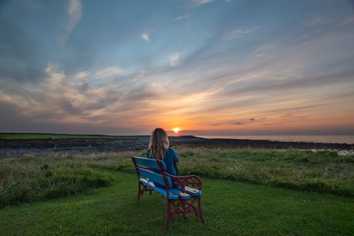An Irish female sitting on a bench looking at a beautiful sunset on the sea coast