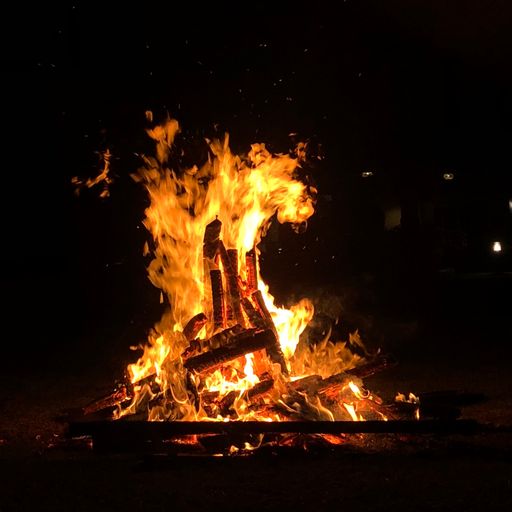A close-up shot of a campfire with flames and smoke at a campsite at night