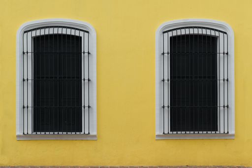 Two windows of a yellow facade and black doors with a metal grille