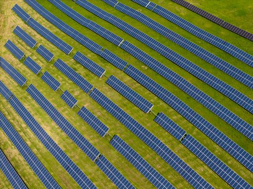 An aerial view of a solar farm with rows of solar panels on a green field