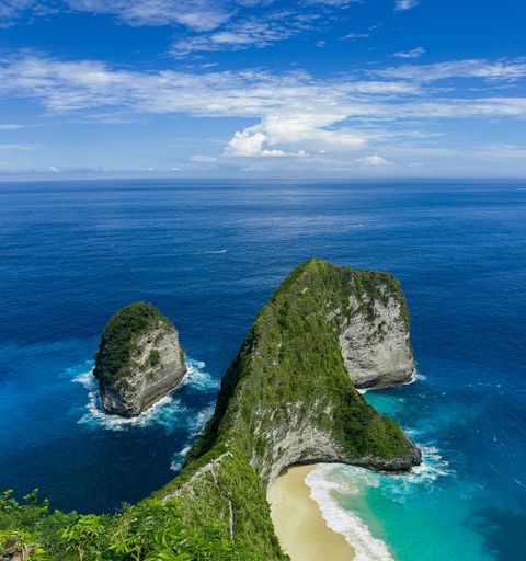 Stunning aerial view of Kelingking Beach on Nusa Penida, Indonesia, with turquoise waters and dramatic cliffs under a clear blue sky.