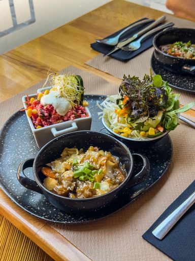 Assorted vegan meal with marinated seitan stew, beet couscous salad and fresh green salad, served on a black ceramic tray over a wooden table.