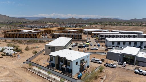 Aerial view of a modern construction site with multiple buildings in a desert landscape under a clear blue sky.