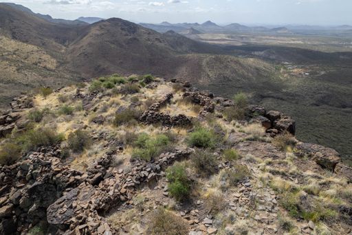 Aerial view of a rugged mountainous landscape with rocky terrain and sparse vegetation under a partly cloudy sky.