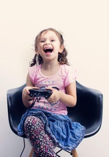 A vertical shot of a Hispanic happy girl playing with the joystick