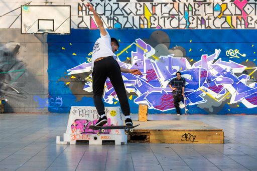 The skateboarders doing tricks in a skate park with bright graffiti in Udine, Italy