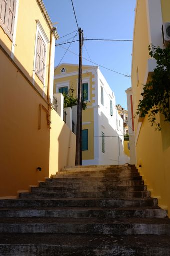 Charming narrow street with colorful buildings and stairs under a clear blue sky in a Mediterranean village.