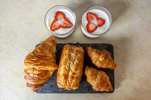 A top view of croissants on a board and two cups of yogurt with strawberries