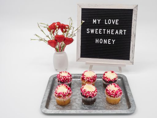 A closeup shot of cupcakes with white and red icing on top with "My love sweetheart honey" text