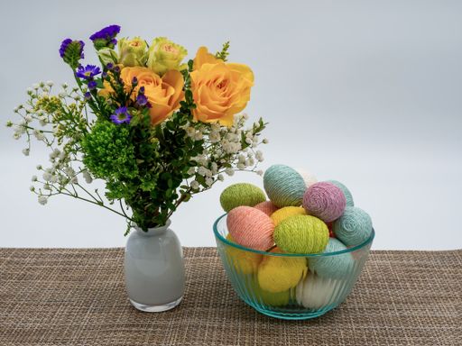 A closeup shot of flowers in a vase with Easter eggs in a bowl on a table