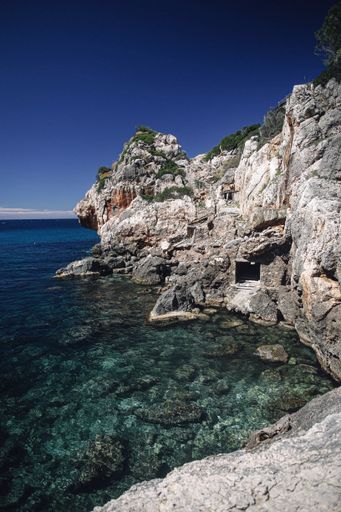 Rocky coastal landscape with clear turquoise waters and rugged cliffs under a deep blue sky, capturing the Mediterranean shoreline.