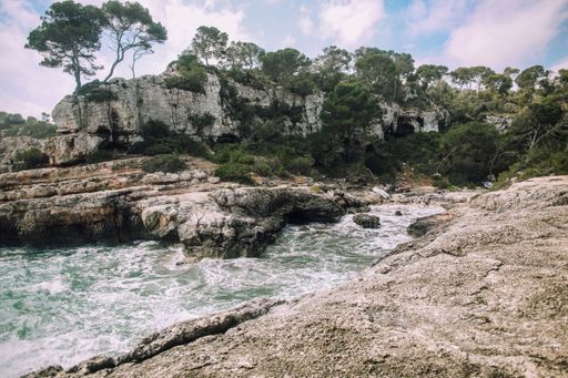Scenic view of rocky coastline with lush green trees and clear turquoise water under a partly cloudy sky.