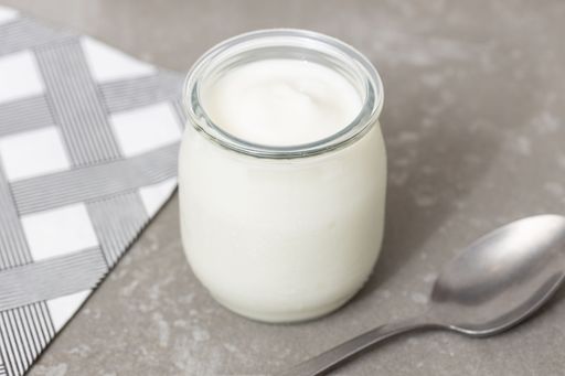 Close-up of a yogurt glass jar on a table with a spoon, a minimalist still life.