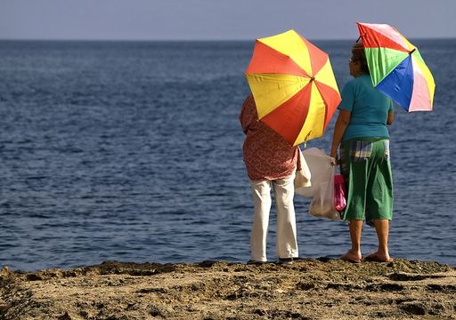 A rear view of two Cuban mothers look at the sea with colorful umbrellas