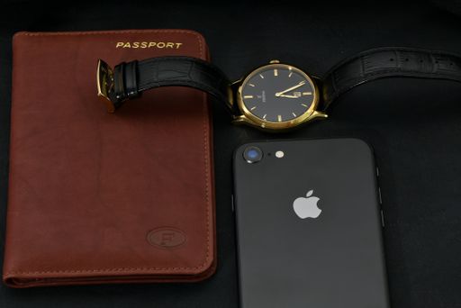 An image of a black Festina leather watch, old iPhone, and leather passport case on a black background