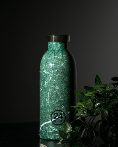 An image of a green marble stainless steel reusable water bottle and decorative plant leaves on a table