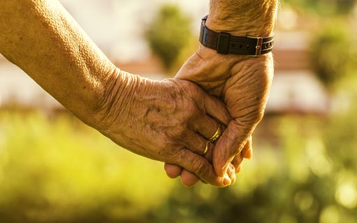 A closeup of an old couple holding hands under the sunlight with a blurry background