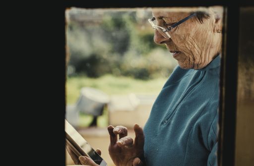 A closeup of an old female with glasses using a smartphone under the sunlight with a blurry background