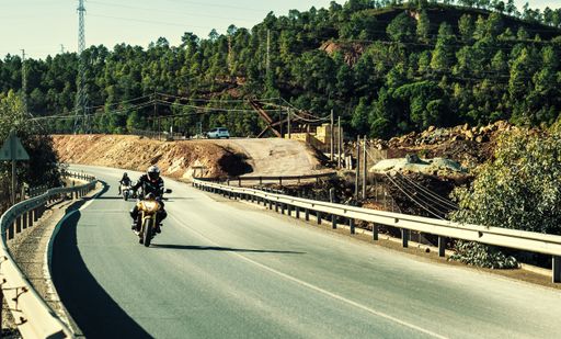 Two people riding motorcycles on the road surrounded by trees under the sunlight in Spain